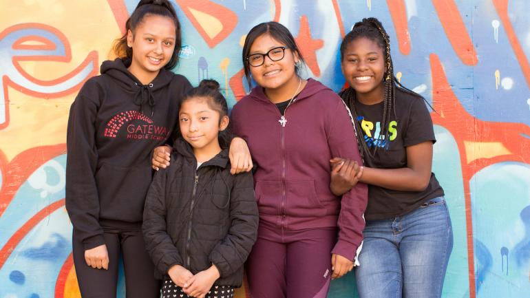 Middle school girls pose in front of a mural